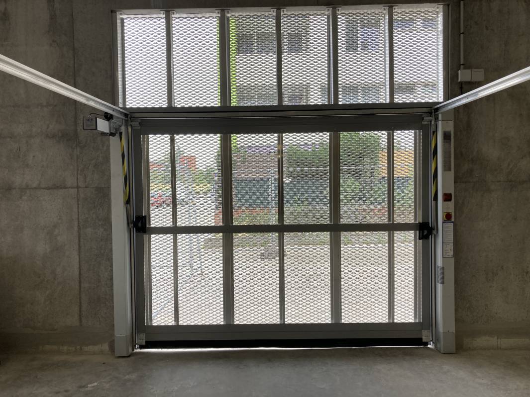 Installation d'une porte basculante collective avec habillage de métal déployé.